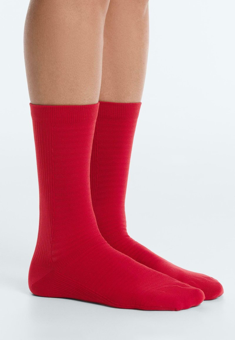 Picioare inferioare purtând șosete roșii aprinse până la jumătatea gambei, stând alături pe o suprafață gri deschis, pe un fundal simplu.