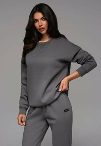 Grauer Sweatshirt und passende Sweatpants aus glattem Stoff, mit Rippbündchen und einem kleinen Logo-Tag an der Hosentasche.