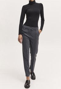 Svart långärmad polotröja i kombination med grå skräddarsydda byxor med framfickor och sidofickor. Svarta loafers fulländar looken.