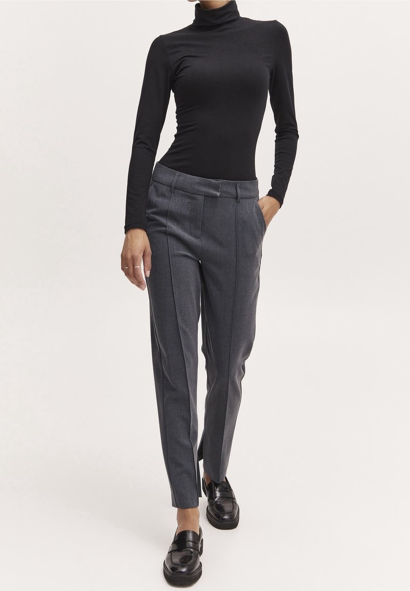 Svart långärmad polotröja i kombination med grå skräddarsydda byxor med framfickor och sidofickor. Svarta loafers fulländar looken.
