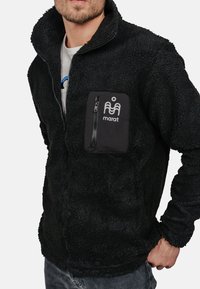 Czarna polarowa kurtka z zapinaną kieszenią na piersi, teksturowany materiał, wysoki kołnierz oraz logo na kieszeni. Materiał nadający się do prania w pralce.