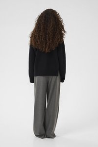 Sweater in black, oversized fit, made of textured fabric. Paired with wide-leg gray trousers, smooth fabric, and relaxed silhouette.