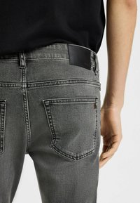 Jeans in denim grigio con un design attillato, dotati di una patch in pelle nera in vita e due tasche posteriori con rifiniture cucite.