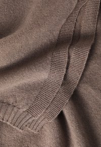 Brązowy sweter z dzianiny z detalem ukazującym miękką fakturę, z prążkowanym mankietem i charakterystycznym wzorem szwu wzdłuż ramion.