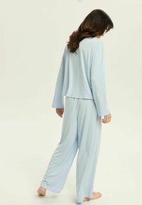 Jasnoniebieski zestaw odzieży domowej z miękkiego materiału; składa się z luźnej bluzki z długim rękawem oraz spodni o szerokich nogawkach z marszczeniami przy mankietach.