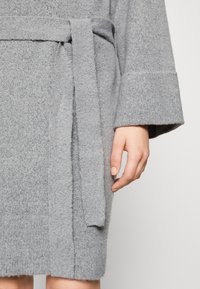 Ropa de punto gris con cinturón, mangas anchas y textura suave. Costillas visibles en el dobladillo, que enfatizan un diseño acogedor.