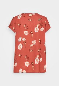 Top a maniche corte color rosso ruggine con un motivo floreale che presenta fiori bianchi e gialli. Materiale morbido, vestibilità rilassata, scollatura rotonda e orlo dritto.