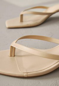 Sandales flip-flop beiges avec une semelle plate, des brides étroites et un design minimaliste avec un léger éclat et des coutures contrastées.