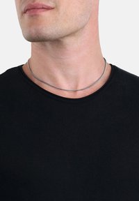 Metallkette mit einer glatten, silberfarbenen Oberfläche, die um den Hals über einem schwarzen Kurzarm-T-Shirt mit Rundhalsausschnitt getragen wird.