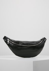 Svart faux krokodil läder midjeväska med en böjd design, framträdande silverdragkedja och en mjuk yta. Justerbar rem ingår.