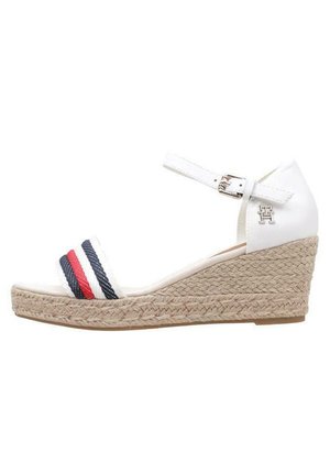 Sandalo bianco a zeppa con suola in juta intrecciata, caratterizzato da accenti a righe blu navy e rosse sulle cinghie. Cinturino alla caviglia regolabile con fibbia metallica.