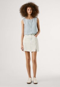 Lichte blauwe cropped denim tanktop gecombineerd met een knielange, crèmekleurige rok met verticale strepen, voorzien van zijsplitten en voorzakken.