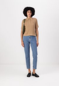 Polo shirt lavorato a maglia di un marrone chiaro con maniche corte, abbinato a jeans azzurri a gamba affusolata e mocassini neri. La camicia presenta un colletto e una texture a coste.