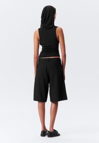 Black sleeveless top with an attached hood, paired with black knee-length shorts. Smooth fabric and simple cut with back pockets.