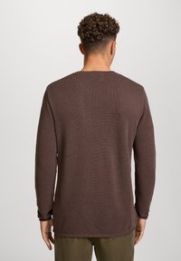 Brązowy sweter z długim rękawem, z teksturowanym, dzianinowym wzorem. Luźny krój z okrągłym dekoltem oraz widocznymi szwami na mankietach i krawędzi.