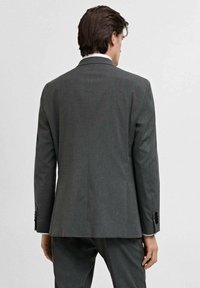 Giacca di abito grigio su misura con una texture liscia. Presenta revers a taglio, uno spacco singolo e dettagli con bottoni neri sui polsini.
