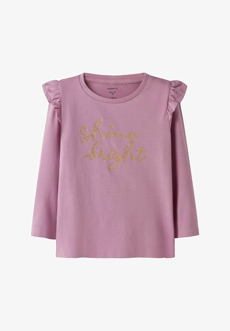 Svijetlo ružičasta košulja dugih rukava s naboranim rukavima. Ima zlatni gliter tekst koji glasi "sjaji sjajno". Mekana tkanina, ležeran dizajn.