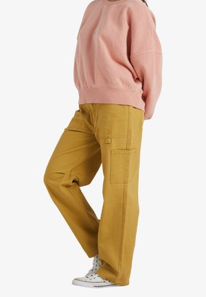 Rosa sweatshirt och senapsgula byxor. Sweatshirten har en rund halsringning och ribbade ärmslut. Byxorna har sidofickor och en avslappnad passform.