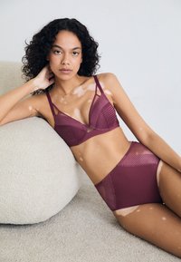 Maroon lingerie set featuring a bralette with mesh and striped accents, paired with high-waisted briefs, against a soft, neutral backdrop.