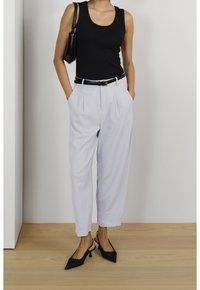 Czarna dopasowana kamizelka w połączeniu z jasnoszarymi spodniami plisowanymi, przewiązanymi czarnym paskiem, oraz czarnymi szpilkami z odkrytą piętą.