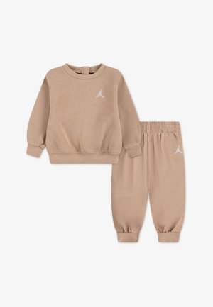 Conjunto de sudadera y pantalones a juego en color beige, hechos de un material suave. Cuenta con puños elásticos y un logo blanco en el pecho y el muslo.