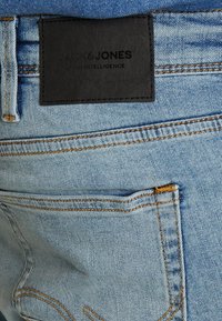 Light blue denim jeans back pocket with orange stitching and black rectangular Jack & Jones brand label above the pocket.