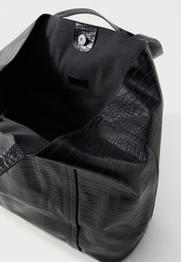 Črna torba iz umetnega usnja s teksturo krokodila. Ima enotno črno notranjost in zapiranje na pokrov. Opremljena je z močnimi ročaji za nošenje.