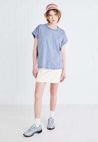 Tricou din bumbac albastru, supradimensionat, cu mâneci rulote, asortat cu o fustă albă din denim. Pantofi sport gri cu accente negre și șosete albe.