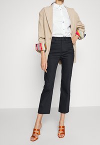 Beige kavaj, vit skjorta med färgglada knappar, svarta skräddarsydda byxor och orange sandaler med två remmar. Minimalistisk och modern design.