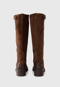 Brown suede knee-high boots with a rounded toe, featuring a short block heel and buckled accents on the sides, smooth texture.