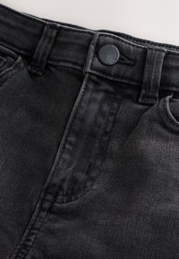 Close-up of black denim jeans waistband showing button, belt loops, front pocket, and detailed stitching.