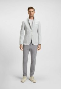 Light gray tailored blazer with a textured finish, two front pockets, and a peak lapel, paired with gray trousers and light sneakers.