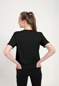 Sort kortærmet t-shirt med rund hals, der har en glat tekstur og en afslappet pasform. Stylet med hænderne i lommerne på sorte jeans.