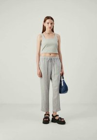 Giovane donna che indossa un top corto grigio chiaro e pantaloni con coulisse, tiene una piccola borsa blu ed indossa sandali neri con_platform.