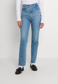 Ljust blå högmidjade jeans med rak passform, som har två framfickor, bälteshällor och knappstängning. I kombination med svarta loafers.