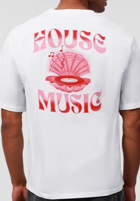 Valge puuvillane T-särk, millel on suur punane ja roosa graafika merikilpkonnast, mille sees on vinüülplaat ja muusikanooled. Särgil on tekst "HOUSE MUSIC".