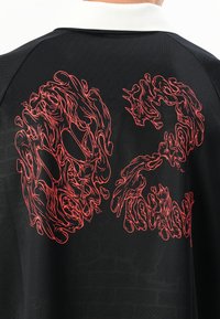 Black polo shirt with a white collar features a bold, intricate red graphic of abstract shapes resembling faces on the back.