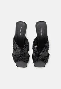 Sandales à talons ouverts noires avec des brides plissées entrelacées et un design à bout carré. Dotées d'une semelle plate et d'une marque Michael Kors sur la semelle intérieure.