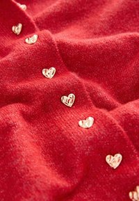 Red knitted fabric with a soft texture, featuring small gold metal heart-shaped embellishments sewn into the material.