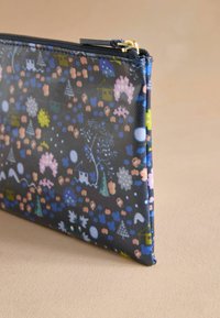 Fodral med dragkedja i texturerad tyg, med ett flerfärgat mönster av träd, hus och blommor på en mörk bakgrund. Guldaccent på hårdvaran.