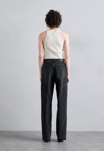 Pantalon en denim noir avec une coupe loose et des détails de couture visibles. Ensemble associé à un débardeur crème à côtes avec un design de couture unique.