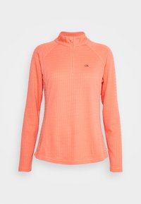 Pull-over à manches longues couleur pêche en tissu texturé, avec un col à demi-fermeture éclair et un logo discret sur la poitrine.