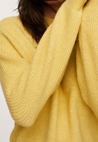 Pull jaune tricoté avec côtes texturées, présentant une coupe ample et des manches larges. Le tissu semble doux et confortable sans motif visible.