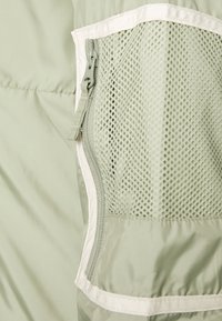 Tela verde claro con un bolsillo de malla con cremallera que presenta un ribete blanco en una prenda o bolsa.