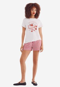 Hvid bomulds t-shirt med rød kage grafik, parret med rød og hvid ternet shorts. Sorte flade sko fuldender outfittet.