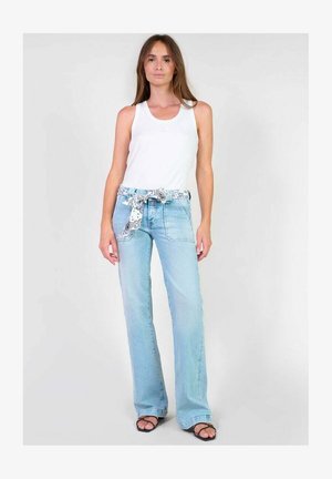 Jeans a zampa d'elefante di colore blu chiaro con una cintura anteriore in tessuto a fantasia e tasche frontali, abbinati a una canotta bianca e sandali neri.