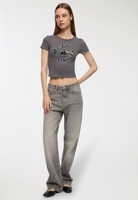 T-shirt grigia cropped con grafica "Pink Floyd 1973 U.S. Tour", abbinata a jeans larghi grigio chiaro. Texture liscia, hardware minimale.