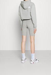 Sudadera gris recortada y pantalones cortos de ciclismo grises, combinados con zapatillas blancas y plateadas. Los calcetines son blancos con letras azules.