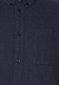 Camicia blu navy con bottoni in un tessuto testurizzato, dotata di una tasca sul petto e sei bottoni neri lungo il patta anteriore.