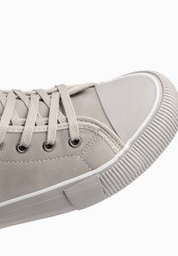 Lichtgrijze sneaker met een glad leren bovenwerk, ronde neus, zes veterogen en een getextureerde rubberen zool met uitgesproken groeven.
